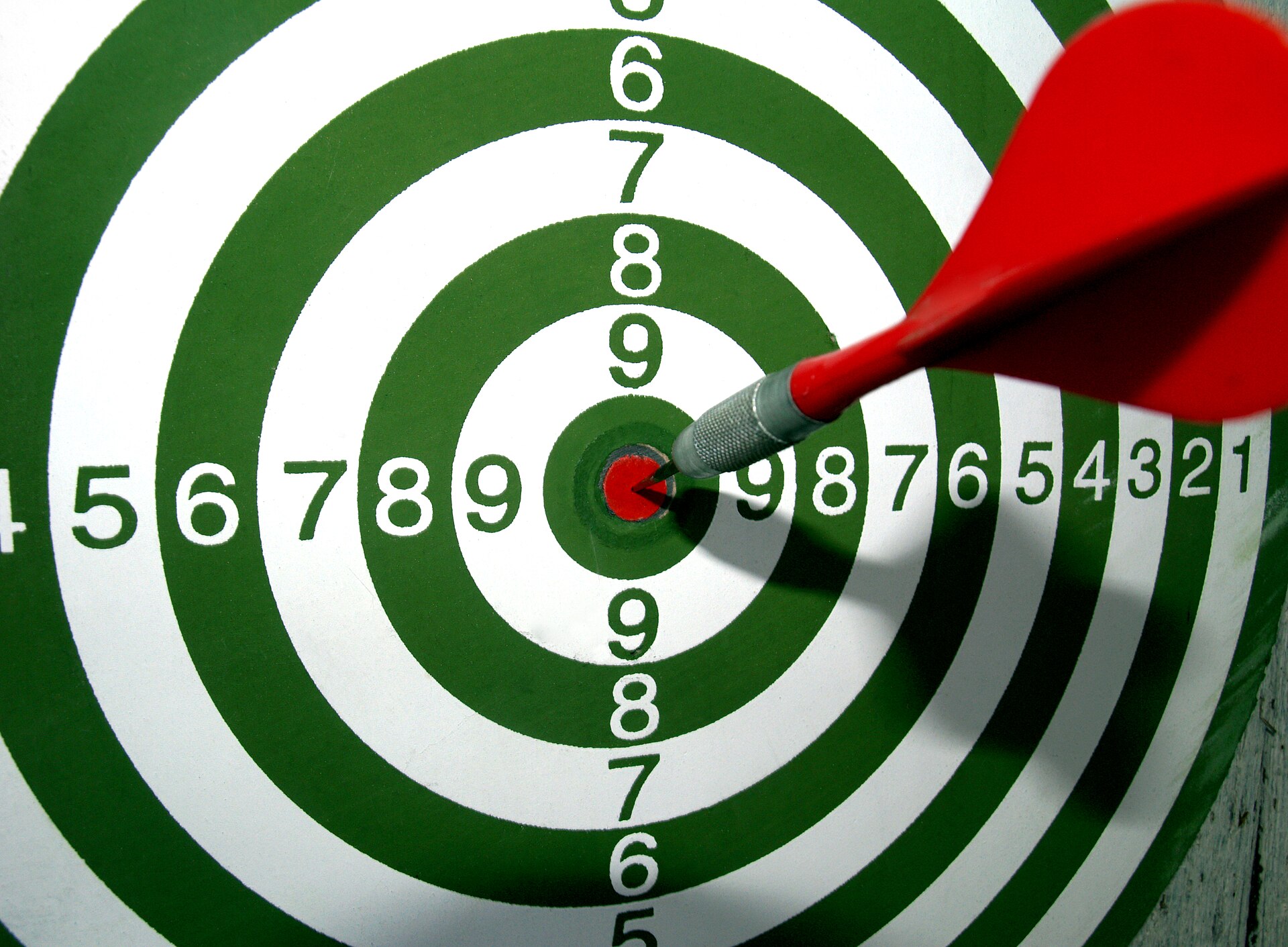 A red dart precisely in the bullseye of a dartboard.
